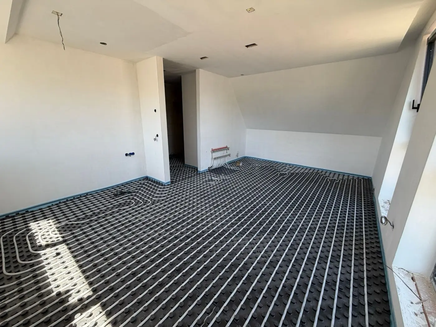 Vloerverwarming op noppenplaten op een zolderverdieping, met de verdeler tegen de wand